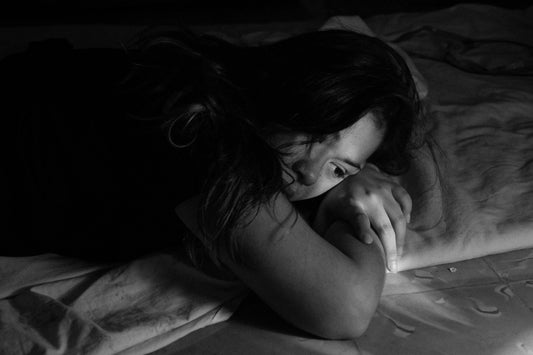 Erschöpft wirkende Frau liegt mit gekreuzten Armen, Schwarz-Weiß-Fotografie